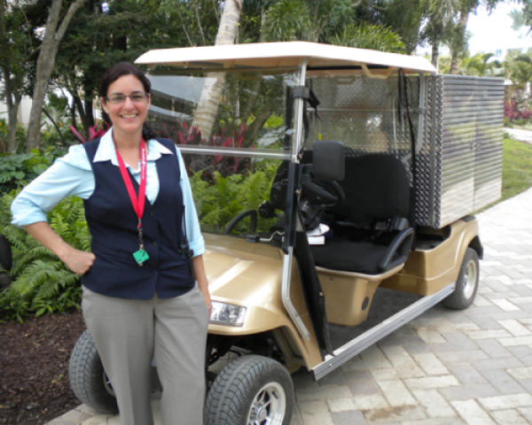 A woman is standing in front of a gold-colored Star electric vehicle while outside.