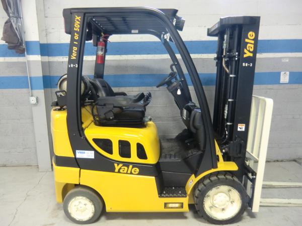 A yellow and black Yale forklift that is parked in front of a grey warehouse wall with blue trimmed stripes.