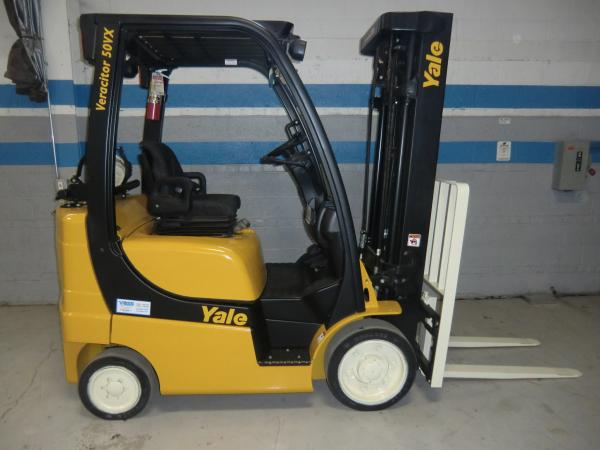 A yellow and black Yale forklift that is parked in front of a grey warehouse wall with blue trimmed stripes.