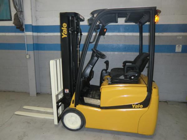 A yellow and black Yale forklift that is parked in front of a grey warehouse wall with blue trimmed stripes.