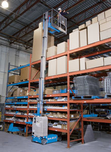 A person working in a warehouse while fully extended in the air by a blue crane lift.