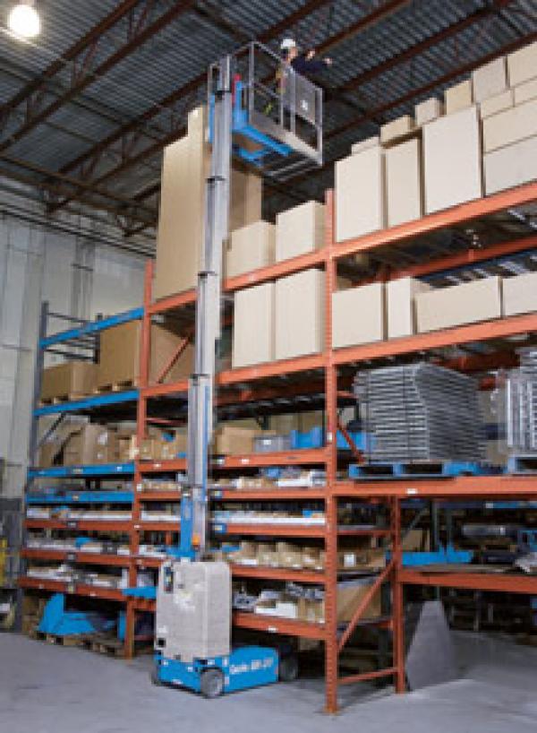 A person working in a warehouse while fully extended in the air by a blue crane lift.