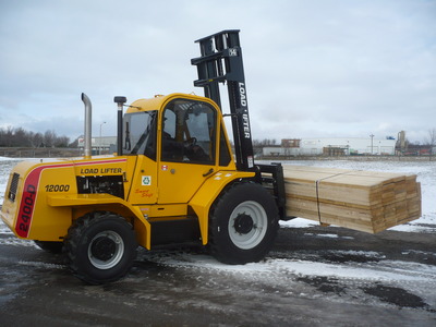 A black and yellow forklift is outside in the snow while handling a pile of wood